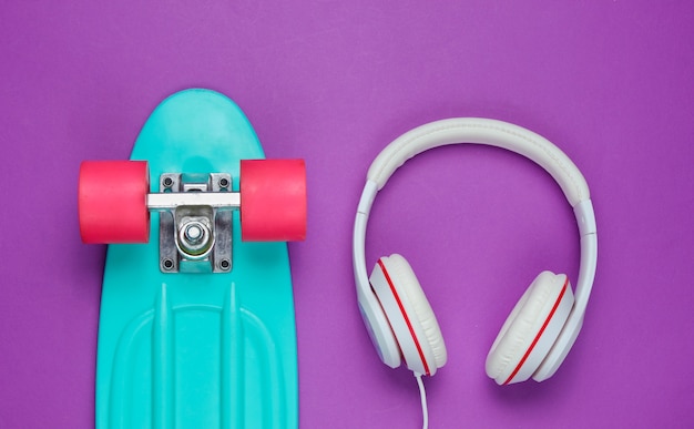 Traje de hipster. Patineta con auriculares sobre fondo morado. Minimalismo de moda creativa. Estilo de moda antiguo de moda. Diversión mínima de verano. Concepto musical