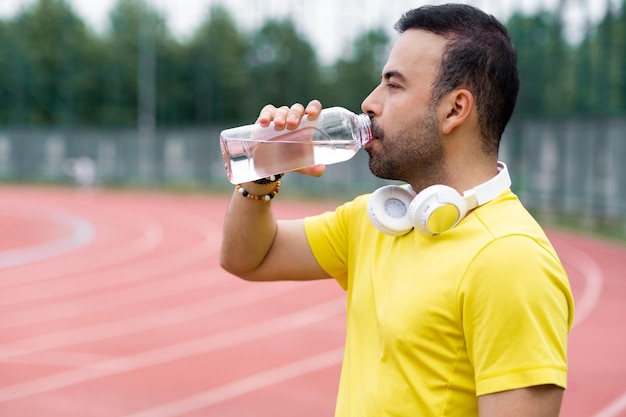 Con trajes amarillos en el hombre atlético toma un descanso hidratando con botella de agua clara arena deportiva