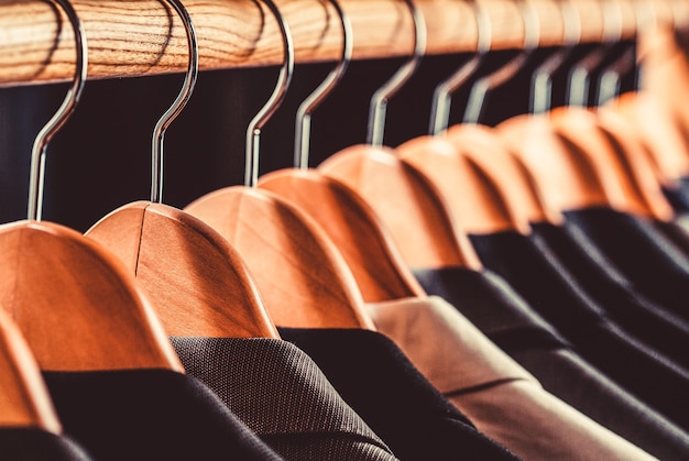 Trajes de hombre en diferentes colores colgando de la percha en una tienda de ropa minorista, primer plano. Camisas de hombre, traje colgado en una rejilla.