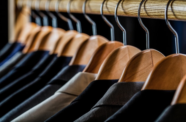 Trajes de hombre en diferentes colores colgando de la percha en una tienda de ropa minorista, primer plano. Camisas de hombre, traje colgado en una rejilla.