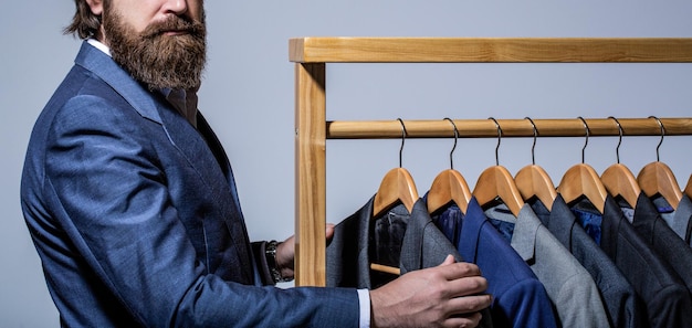 Trajes masculinos colgando en una fila Boutiques de ropa para hombres Sastre de traje de hombre en su sastrería Taller de traje de hombre elegante Guapo hombre de moda barbudo en traje de traje clásico