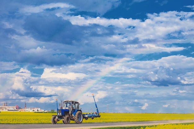 Traktor fährt in der Nähe des Feldes mit einem Regenbogen