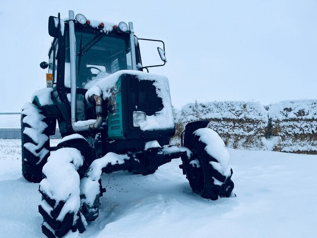 Traktor in der Wintersaison auf dem Feld in der Nähe von Heu geparkt Ackerschlepper steht bei schneebedecktem und bewölktem Wetter