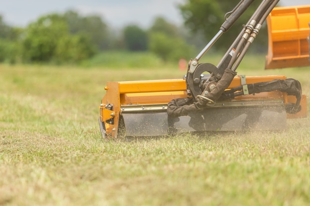 Traktor mit einem mechanischen Mäher, der Gras auf der Seite der Asphaltstraße mäht