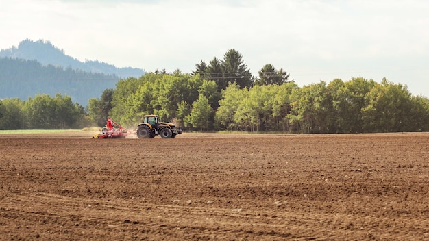 Traktor sät auf leerem Feld auf dem Land, kleine Bäume im Hintergrund.