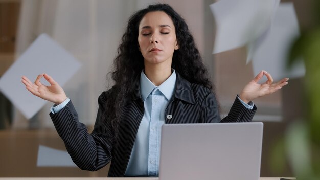 Foto tranquila y consciente jefa de mujer de negocios en posición de loto tomando un descanso meditando el fondo de