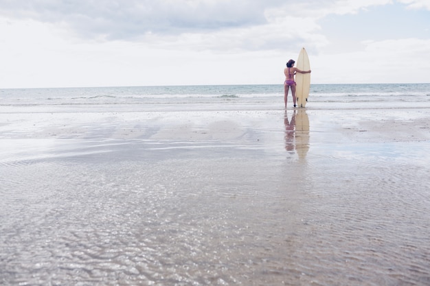 Tranquila mujer en bikini con tabla de surf en la playa