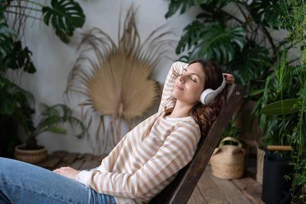 Tranquila mujer joven soñando despierta usando auriculares en plantas de armonía escuchando música o audiolibro