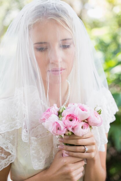 Tranquila novia con velo sobre la cara con ramo de rosas