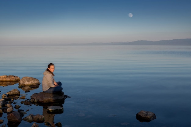 Tranquila puesta de sol sobre el río. La niña está sentada sobre una piedra grande.