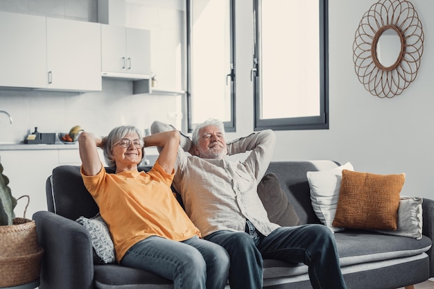 Tranquilo hombre y mujer de mediana edad con los ojos cerrados relajándose en un cómodo sofá en casa familia madura soñando juntos esposa y esposo de cabello gris descansando con las manos detrás de la cabeza respirandoxA