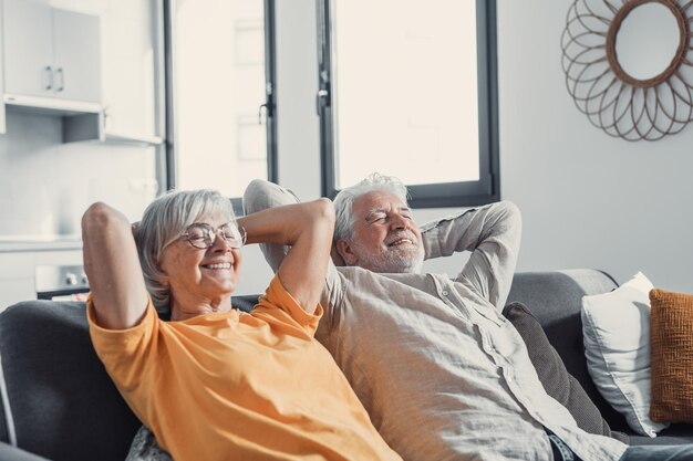 Tranquilo hombre y mujer de mediana edad con los ojos cerrados relajándose en un cómodo sofá en casa familia madura soñando juntos esposa y esposo de cabello gris descansando con las manos detrás de la cabeza respirandoxA