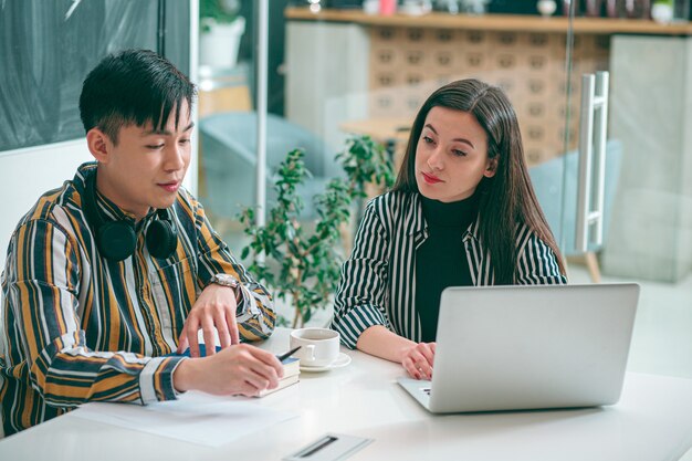 Tranquilo joven y mujer que tienen una conversación en el trabajo mientras están sentados a la mesa