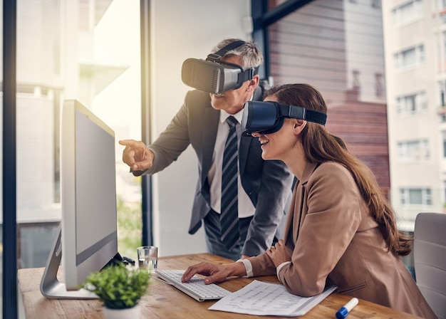 Transferindo suas ideias por meio de novas dimensões Foto de dois empresários usando fones de ouvido VR enquanto trabalhavam em um computador em um escritório