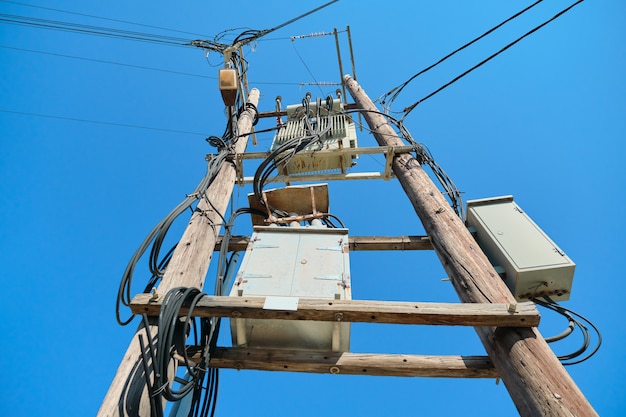 Transformador elétrico em postes de madeira, fundo de céu azul.