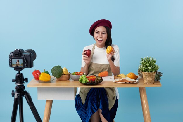 Foto transmisión en vivo de una joven asiática que muestra frutas y verduras frente a la cámara