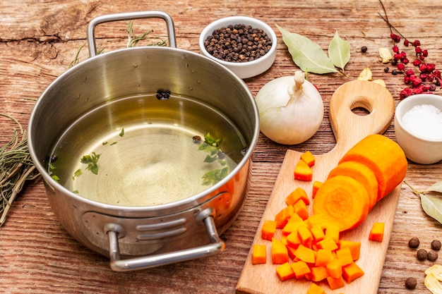 Transparente Entenbrühe in der Pfanne mit frischen Zutaten. Traditionelle Bouillon für gesunde Gerichte. Gewürze, Gemüse, alter Holztisch