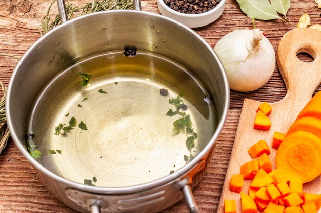 Foto transparente entenbrühe in der pfanne mit frischen zutaten. traditionelle bouillon für gesunde gerichte. gewürze, gemüse, alter holztisch