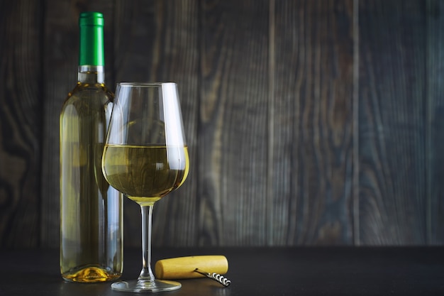 Transparente Flasche trockener Weißwein auf dem Tisch. Weißweinglas auf einem hölzernen Wandhintergrund.