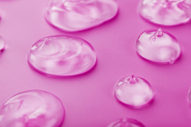 Transparente Gel-Tropfen auf einer rosa Oberfläche