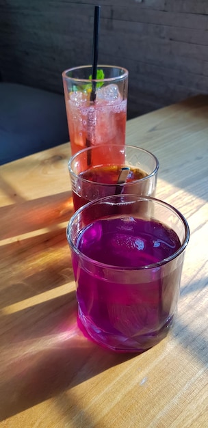 Transparente Gläser mit süßen Getränken im Inneren mit buntem Getränk mit Schatten und Tischhintergrund mit Eiswürfeln