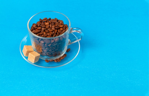Transparente Glasschale mit Kaffeebohnen mit Scheiben des Rohzuckers auf Blau