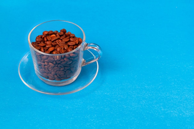 Transparente Glasschale mit Kaffeebohnen mit Scheiben des Rohzuckers auf einem blauen Hintergrund. Kopieren Sie Platz.