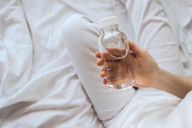 Transparente Öko-Plastikflasche mit Trinkwasser in Frauenhänden