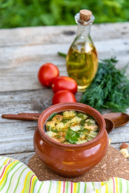 Transparente Suppe in einem Tontopf mit Croutons und Dill nach vegetarischer Art, Flasche mit Öl und Tomaten.