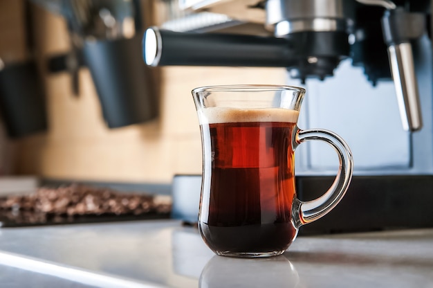 Transparente Tasse Kaffee Nahaufnahme Vorderansicht. Home-Kaffeemaschine und Verfahren zur Herstellung von Kaffeegetränken. Defokussieren Sie von Kaffeebohnen und kopieren Sie Platz.
