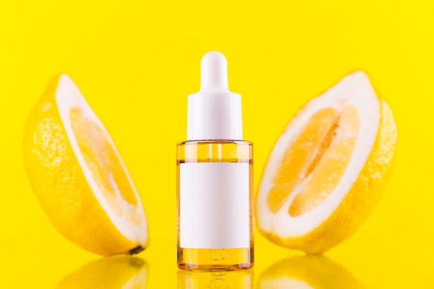 Transparente Tropferflasche für Serum oder Essentials mit Vitamin C Öl Zitrone zwei auf gelbem Hintergrund