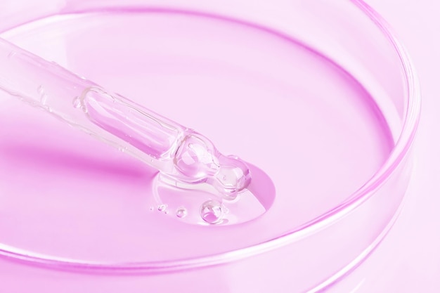 Transparentes Gel, das aus einer Pipette in eine Petrischale fließt, auf rosa Hintergrund, Nahaufnahme