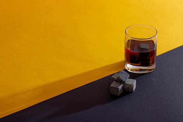 Transparentes Glas mit Whisky auf dunklem Hintergrund mit hellen Lichtstrahlen Whiskysteine in einem Glasglas