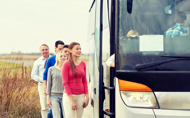 Foto transport-, tourismus-, roadtrip- und personenkonzept - gruppe glücklicher passagiere, die in den reisebus einsteigen