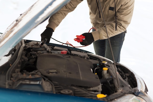 Transport-, Winter- und Fahrzeugkonzept - Nahaufnahme des Mannes unter der Motorhaube mit Starterkabeln