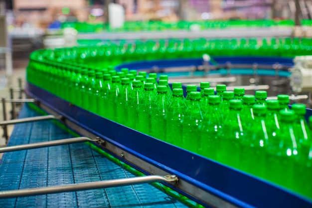 Transportador interior de la fábrica de bebidas que fluye con botellas de jugo verde o agua