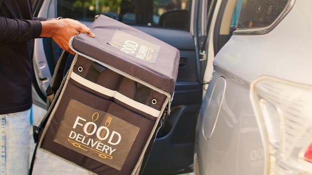 Transportadora afro-americana saindo do carro para entregar pacote de comida, saindo do veículo e dando pedido de fastfood ao cliente. Funcionário do serviço de entrega tocando campainha para entregar o almoço.