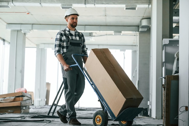 Transportando una larga caja de papel Trabajador de la construcción en uniforme en una habitación vacía sin terminar