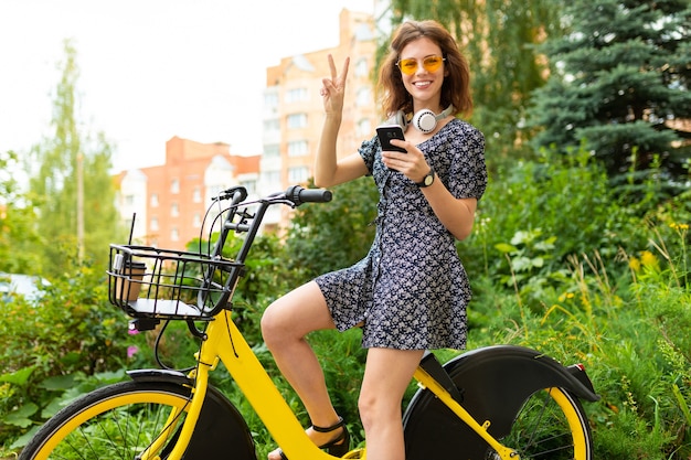Transporte ecológico. linda chica europea monta una bicicleta de alquiler en un parque de la ciudad y allana la ruta por teléfono.