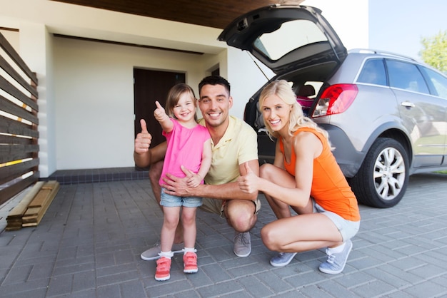 transporte, ocio, viaje por carretera y concepto de personas - familia feliz con una niña pequeña y un camión con puerta trasera que muestra su aprobación en el espacio de estacionamiento en casa