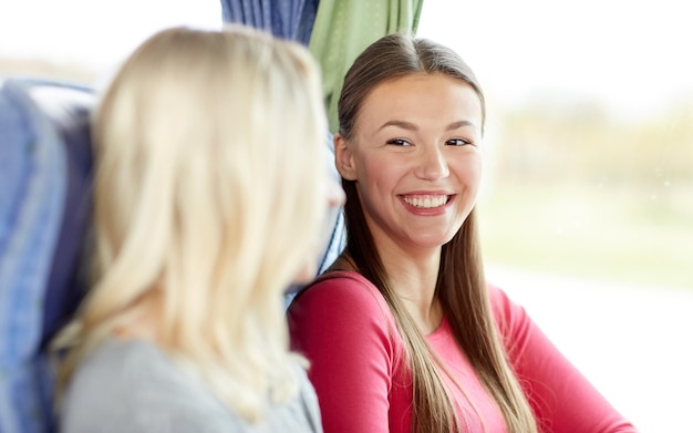 transporte, turismo, amistad, viaje por carretera y concepto de personas - mujeres jóvenes felices sentadas y hablando en un autobús de viaje