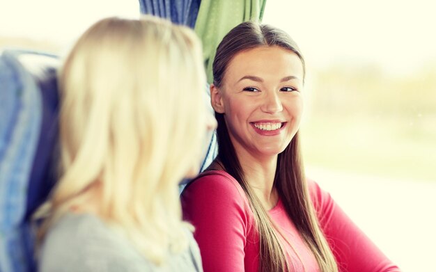 transporte, turismo, amizade, viagem e conceito de pessoas - mulheres jovens felizes sentadas e conversando no ônibus de viagem