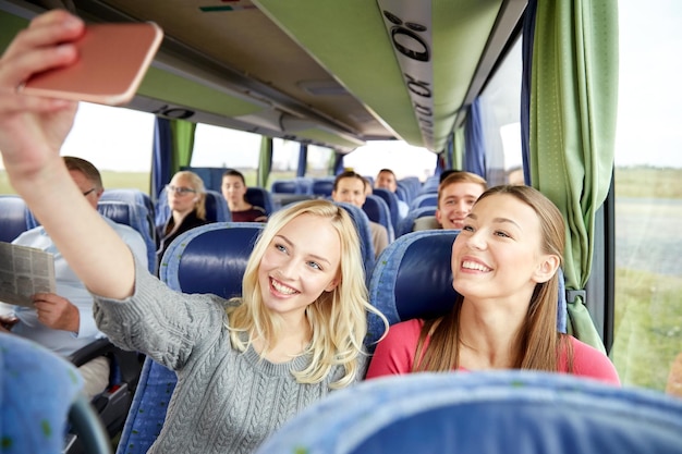 transporte, turismo, viagem e conceito de pessoas - mulheres jovens felizes ou amigos em ônibus de viagem tomando selfie por smartphone