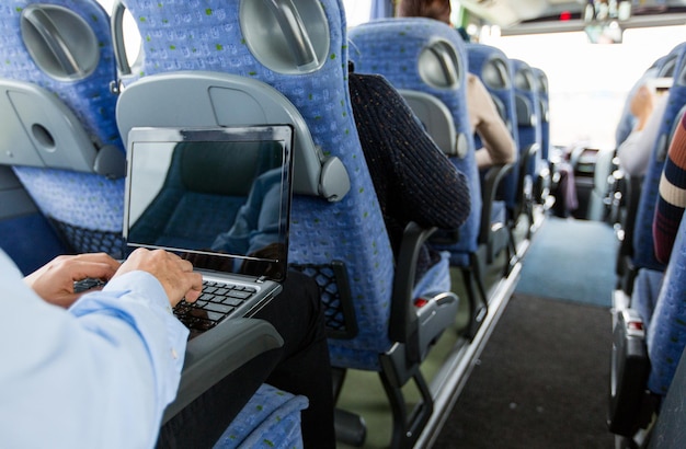 transporte, turismo, viaje de negocios y concepto de personas - cerca de un hombre con una laptop escribiendo en un autobús de viaje