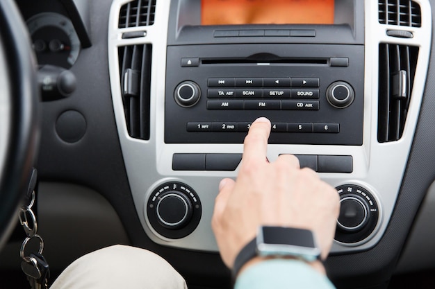 transporte, viagem, condução de carro, tecnologia e conceito de pessoas - close-up da mão masculina ligando o rádio no sistema do painel de controle no carro