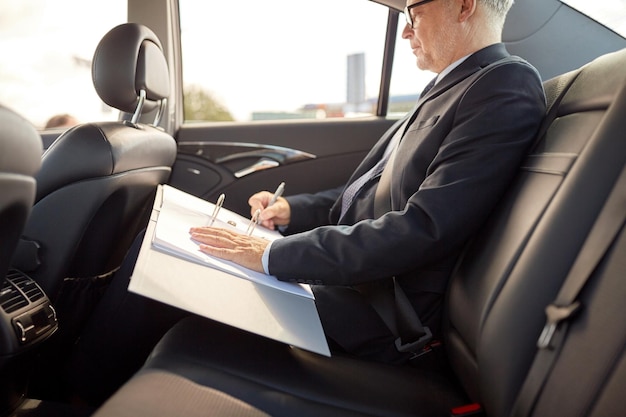 transporte, viagem de negócios, papelada e conceito de pessoas - empresário sênior assinando papéis com caneta e dirigindo no banco traseiro do carro