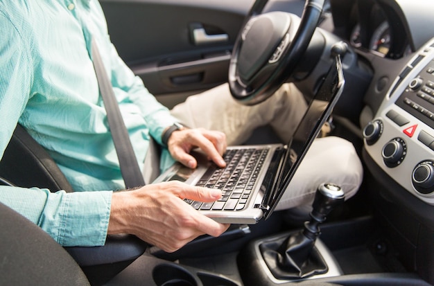 transporte, viaje de negocios, tecnología y concepto de personas - cierre de un joven con un ordenador portátil conduciendo un coche