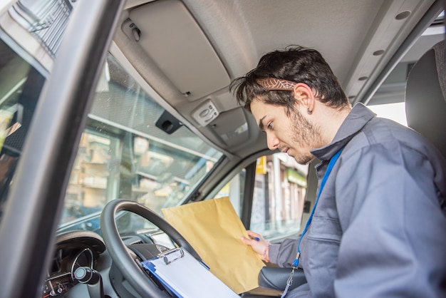 Transportista con uniforme en el asiento del conductor mirando los paquetes para entregar los pedidos