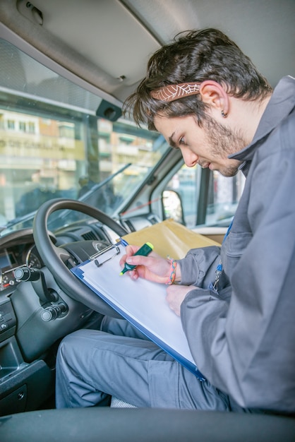 Transportista con uniforme en el asiento del conductor mirando los paquetes para entregar los pedidos