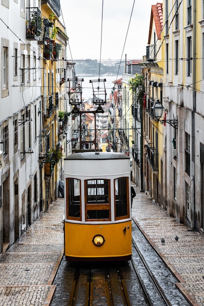 Tranvía amarillo tradicional en una calle estrecha de Lisboa en un lluvioso día de invierno, con el río Tajo desenfocado de fondo.